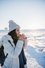 Fototapeta na wymiar beautiful young woman at sunset in snowy mountain holding a cup of hot tea. Travel and Nature concept. winter season