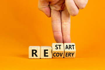 Recovery and restart symbol. Businessman hand turns cubes and changes the word 'recovery' to 'restart'. Beautiful orange background. Business and recovery - restart concept. Copy space.