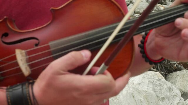 Close up of hands with bracelets play the violin. Playing violin as the guitar.