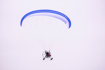 Motor speed paraglider flying in the dim and gloomy sky in winter