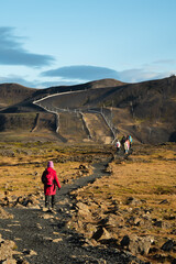 Rear view portrait of a traveler walking on the trail across lava fields, back from Iceland's Thrihnukagigur volcano. Red jacket girl hikes towards mountain at autumn. Inside the Volcano tour