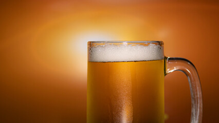 Pour the beer into a clear glass with beer foam and bubble. Golden orange light background.