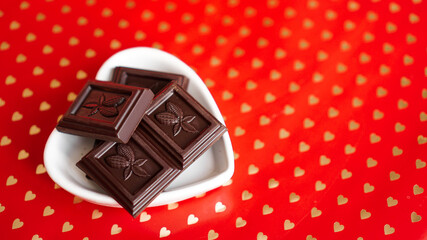 Black chocolate in a heart shaped plate on red background