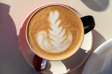 Cup of cappuccino, latte art design, drawing on foam, close-up, on a table in a street cafe on a sunny day. Concept hot drinks, cow's milk substitutes
