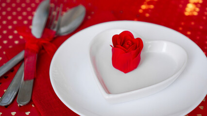 Romantic decoration of holiday table. White plates in the shape of a heart with a red rose. Red background