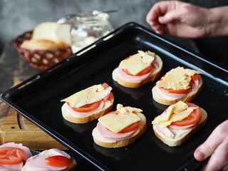 Female hands hold a black baking sheet with sandwiches prepared for baking in the oven. Confectionery background.