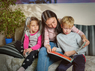 Girl nanny reads a book to children. Working with children at home. Education and pastime with...