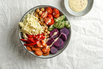 budha bowl with purple batata, bell peppers, cabbage, sweet potatoes, chickpeas, cucumbers on the white linen tablecloth