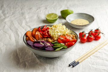 budha bowl with purple batata, bell peppers, cabbage, sweet potatoes, chickpeas, cucumbers on the white linen tablecloth