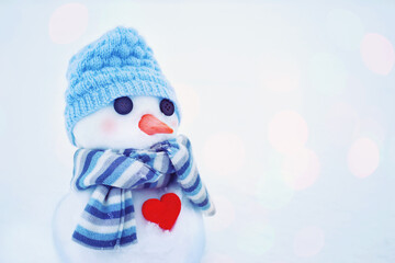 Little cute snowman in a hat and a scarf with red heart in the snow, close-up. Holiday card with a snowman	