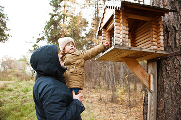 Father and son feed the birds in the autumn forest. Very beautiful wooden bird feeder.