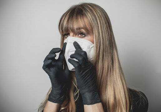 young, blond beautiful woman puts ffp2 protective mask on with protective medical gloves for protection against corona