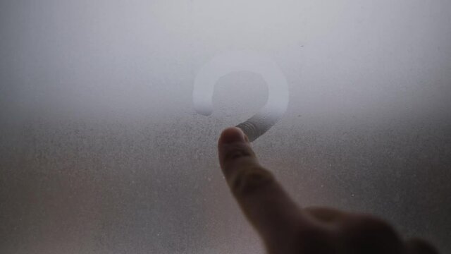 Draws a question mark on the window with your finger. The window was fogged up. Drawing on the wet glass of a window on a gloomy day, isolated at home. Gray colors