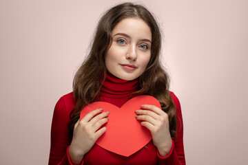 Young girl showing red heart from cardboard to camera