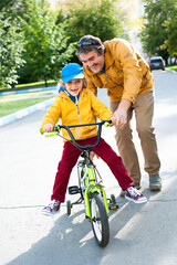 The father teaches his son to ride a Bicycle. Dad and son spend time together.