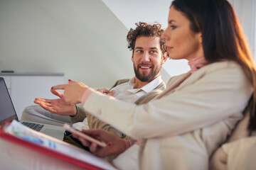 Fototapeta premium Cheerful business couple sitting and discussing on the couch in a an apartment. Business, couple, leisure, together