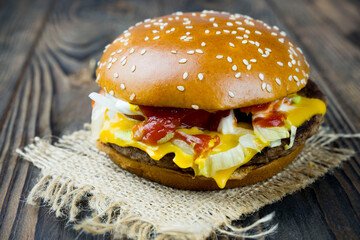 Close-up of a delicious fresh homemade burger with lettuce, cheese, onions and tomatoes on a wooden table, the concept of a mouth-watering meal