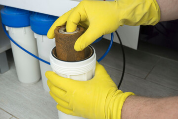 Plumber in yellow household gloves changes water filters. Repairman installing water filter...