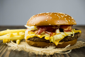 Close-up of a delicious fresh homemade burger with lettuce, cheese, onions and tomatoes on a wooden table, the concept of a mouth-watering meal