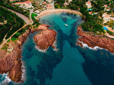 Aerial view of a small beach with turquoise waters, anchored small boat and red rocks, typical of the Esterel close to Cannes. picture taken in Agay, French Riviera, Côte d'Azur south of France