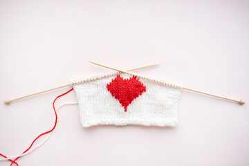 knitted red heart on pink background. Wooden knitting needles. Valentine day.
