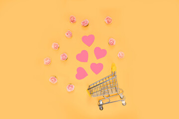 A cart with scattered pink hearts and small roses on a bright yellow background. Valentine's day gift concept. view from above. copy space. Flat lay