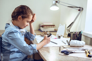 Obraz premium Smilling Caucasian teenage girl in headphones is learning distant form home using smartphone.