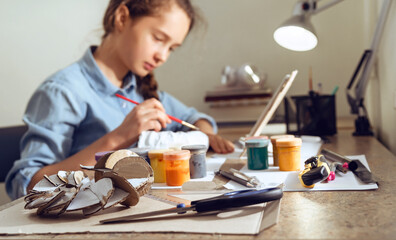 Teenager girl painting with colors, sitting at home at the table.