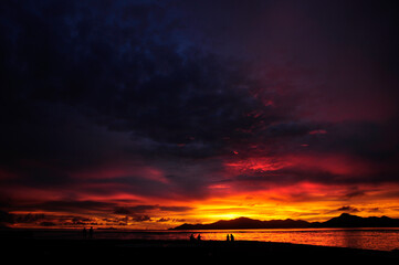 Fototapeta premium Stunning and colourful sunset with overcast sky over the Indian Ocean with silhouette of an island and reflection on the sea. Seychelles