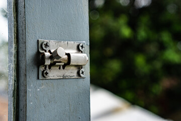 Door slot lock padlock screwed into a window wood frame. The lock made from stainless steel silver metal.