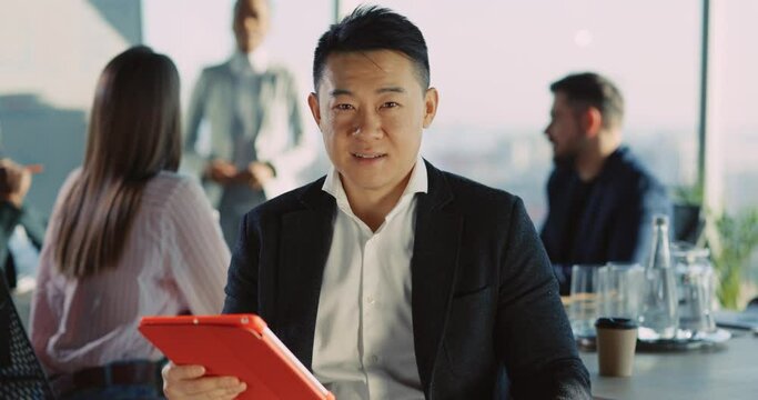 Face of handsome susccessful chinese asian young businessman holding tablet computer attending corporate meeting in office company. Multi-ethnic people.