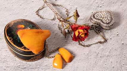 Old yellow Baltic amber brooch on a black painted metal box on a gray plastered surface. Retro...