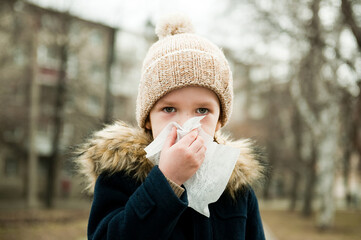 The child blows his nose in a handkerchief outside.
