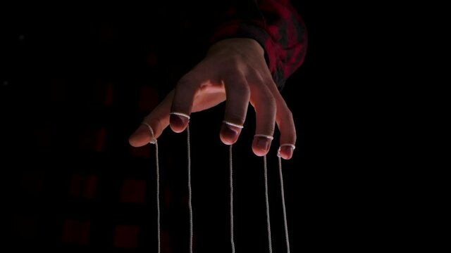 Man holding a puppet string. Close up human hand controls a puppet with fingers attached to strings, on a black background. Control concept. Slow motion.