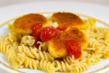 Homemade dinner of boiled pasta with nuggets and ketchup.