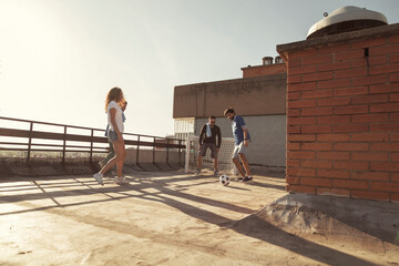 Group of friends having fun playing football on building rooftop terrace