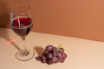 Brunch of red grapes and glass of red wine on beige background with shadow on the wall. Winery concept. View from above.