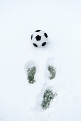 Classic soccer ball on a snowy sports field and footprints in the snow. Copy space, vertical orientation  © Serhii