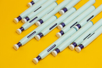 Seamless yellow paper background with an amount of syringe pens. Studio medical equipment still life concept with auto-injector disposable devices.