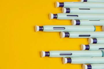 Used self applicant syringe pens forming a pattern on seamless yellow background. Studio medical equipment still life concept with auto-injector disposable devices. © Maarten Zeehandelaar