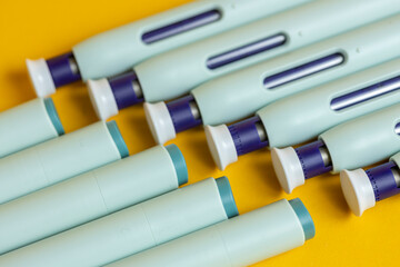 Top and bottom ends of self applying medication syringe pen filling the frame on seamless yellow backdrop. Studio medical equipment still life concept with auto-injector disposable devices. © Maarten Zeehandelaar