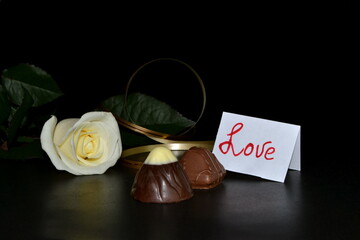 White rose, chocolate candy and golden ribbon on a black background.