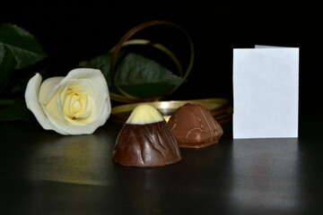 White rose, chocolate candy and golden ribbon on a black background.