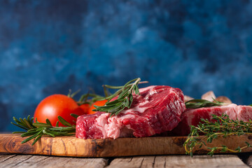 Composition with raw pork meat with tomatoes and rosemary on wooden cutting board o blue...