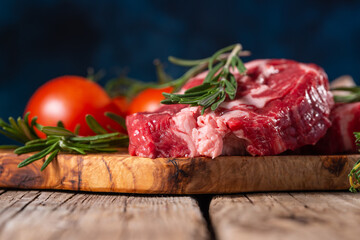 Macro shot of raw pork or beef meat with tomatoes and rosemary on wooden cutting board o blue background. Image for butcher shop. Appetizing view for advertising. - obrazy, fototapety, plakaty