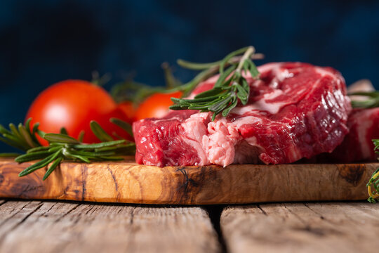 Macro shot of raw pork or beef meat with tomatoes and rosemary on wooden cutting board o blue background. Image for butcher shop. Appetizing view for advertising.