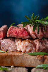 Macro shot of medium rare grilled juicy beef steak ribeye with rosemary on wooden cutting board on dark blue background. Appetizing image for restaurant menu. Delicious food.