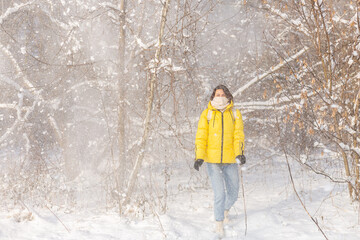 Beautiful young cheerful woman in a snowy landscape winter forest having fun rejoices in winter and snow in warm clothes, scarf and jeans
