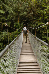 Obraz premium Hispanic young man walking on a suspension bridge in the middle of the forest - Young traveler walking while observing nature and enjoying the ride - Adventurous man