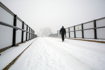 M in black clothes crossing a bridge covered in snow in Franconia, a region in the state of Bavaria in Germany 